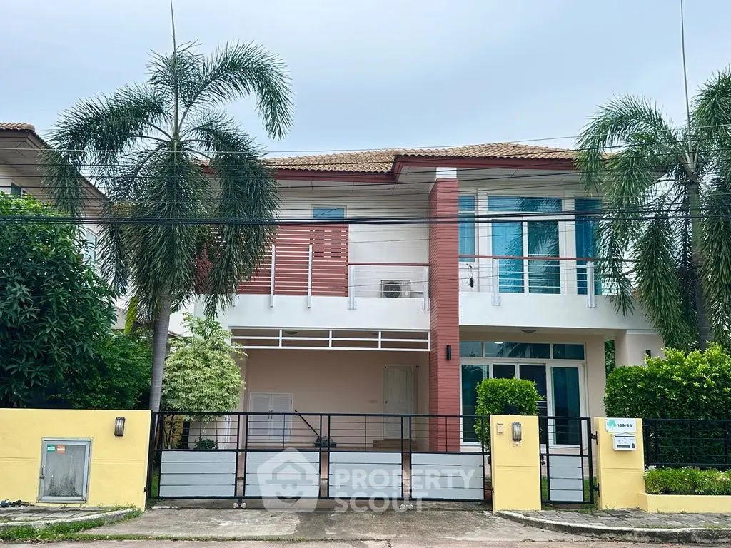 Charming two-story house with tropical landscaping and gated entrance in a serene neighborhood.