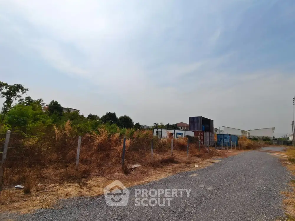Vacant land plot with gravel road and shipping containers, ideal for development opportunities.
