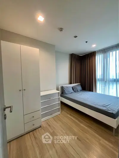 Modern bedroom with wooden flooring, large window, and minimalist furniture