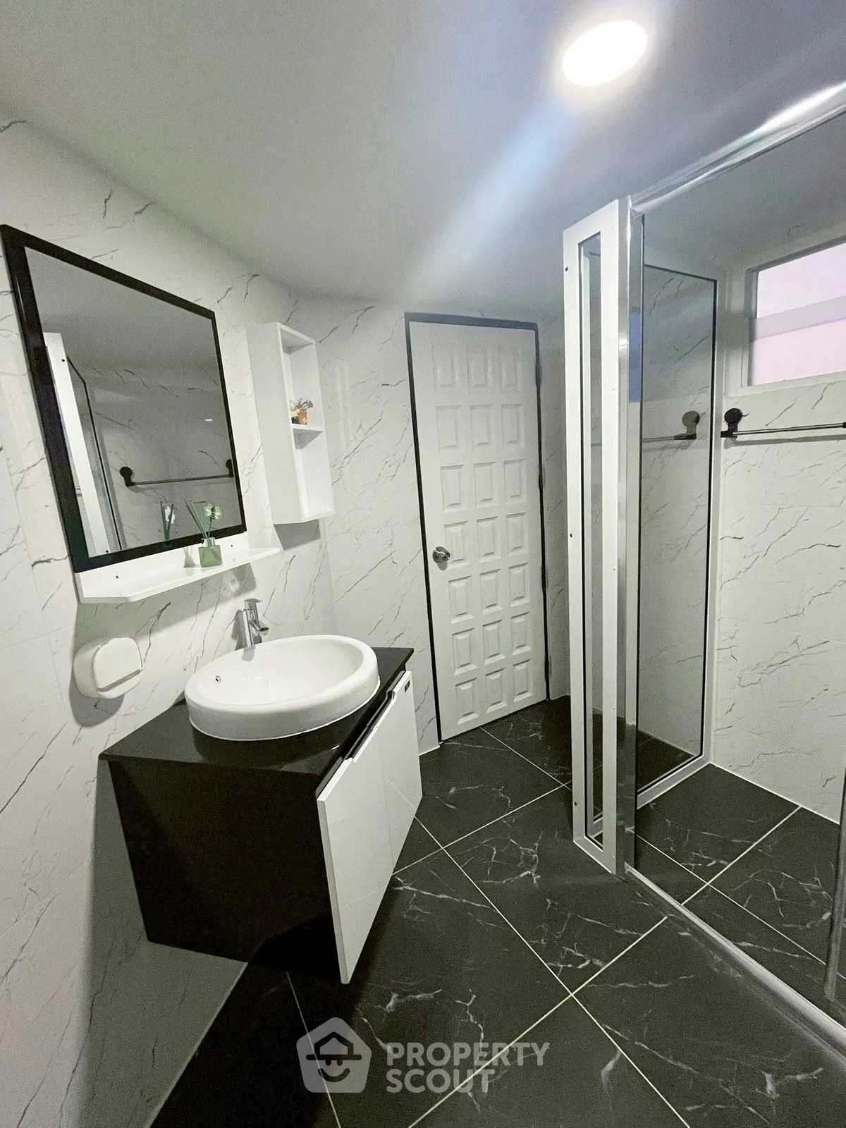 Modern bathroom with sleek black and white design, featuring a stylish sink and glass shower enclosure.