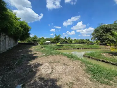 Expansive outdoor land with lush greenery and serene pond under a bright blue sky.