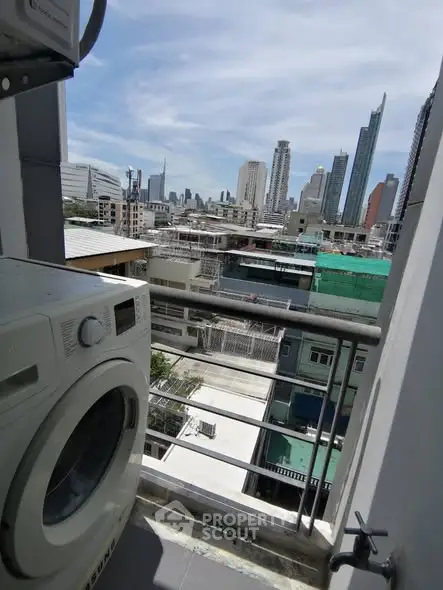 City view from balcony with washing machine, showcasing urban skyline.