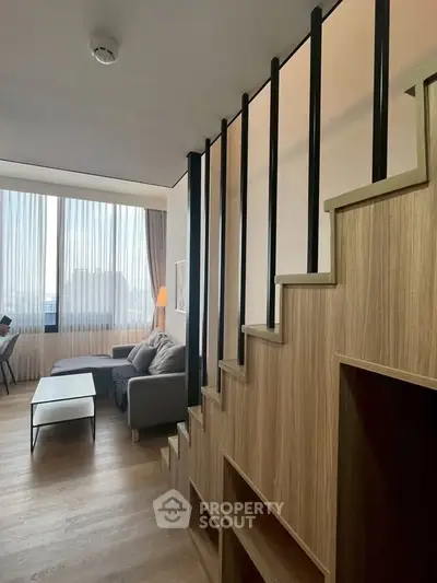 Modern living room with stylish staircase and large windows offering natural light.