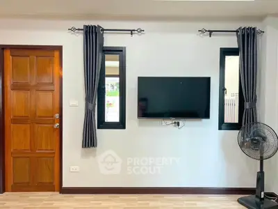 Modern living room with wall-mounted TV and stylish curtains, featuring a wooden door and sleek flooring.