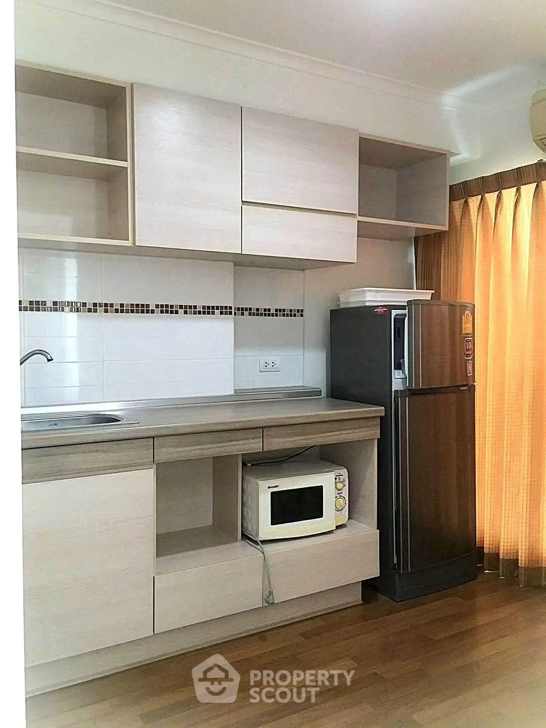 Modern kitchen with sleek cabinetry, microwave, and fridge in a cozy apartment setting.