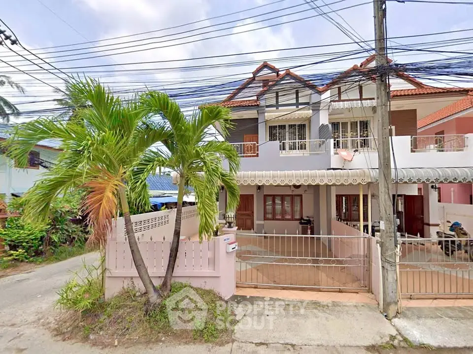 Charming two-story house with gated entrance and lush palm tree in a suburban neighborhood.