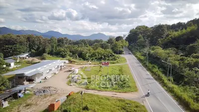 Scenic aerial view of a rural road with lush greenery and distant mountains, ideal for real estate development.