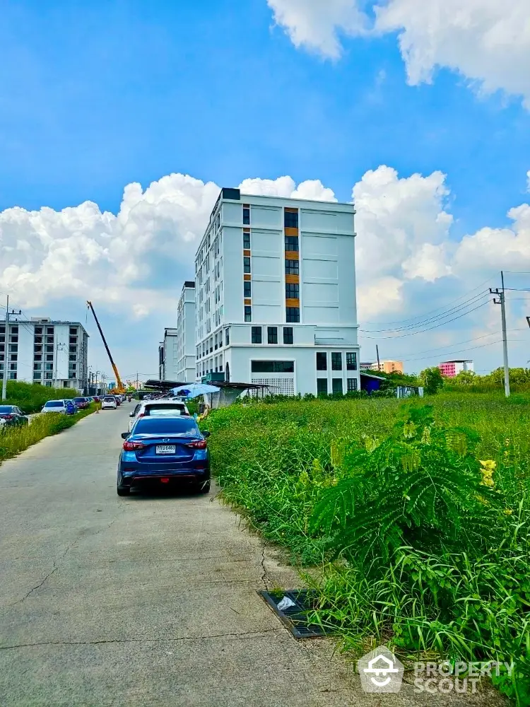 Modern multi-story residential building with ample parking, set against a blue sky with lush greenery in the foreground, offering a blend of urban living and nature.