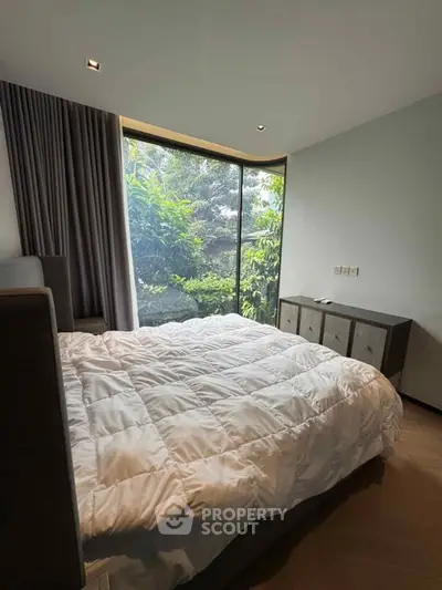 Cozy bedroom with large window and lush garden view, featuring modern furniture and soft lighting.