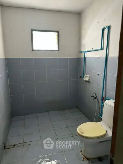 Simple bathroom with blue tiles and a small window, featuring basic plumbing fixtures.