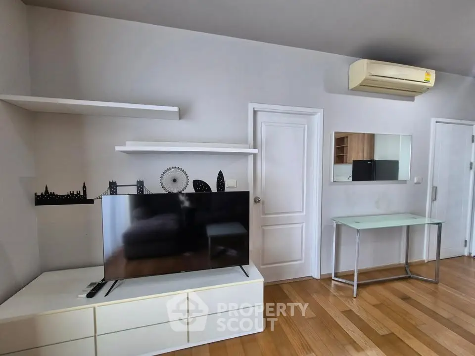 Modern living room with sleek TV setup and air conditioning, featuring wooden flooring and minimalist decor.