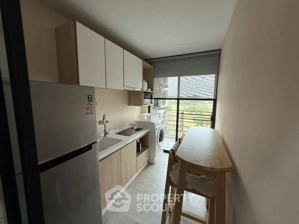 Modern kitchen with sleek appliances and natural light, featuring a washing machine and breakfast bar.