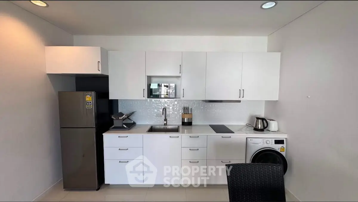 Modern kitchen with sleek white cabinets, stainless steel fridge, and washing machine in a compact layout.