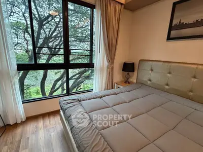 Cozy bedroom with large window offering serene tree views, featuring a plush bed and elegant decor.