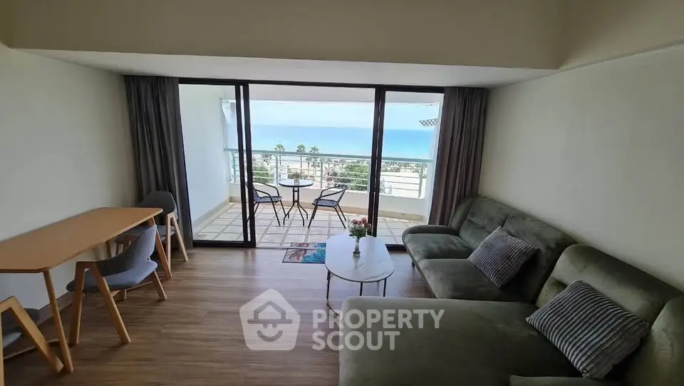Spacious living room with ocean view and large balcony, modern furniture, and wooden flooring.