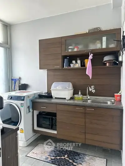 Modern kitchen with wooden cabinets and washing machine, featuring open layout and natural light.