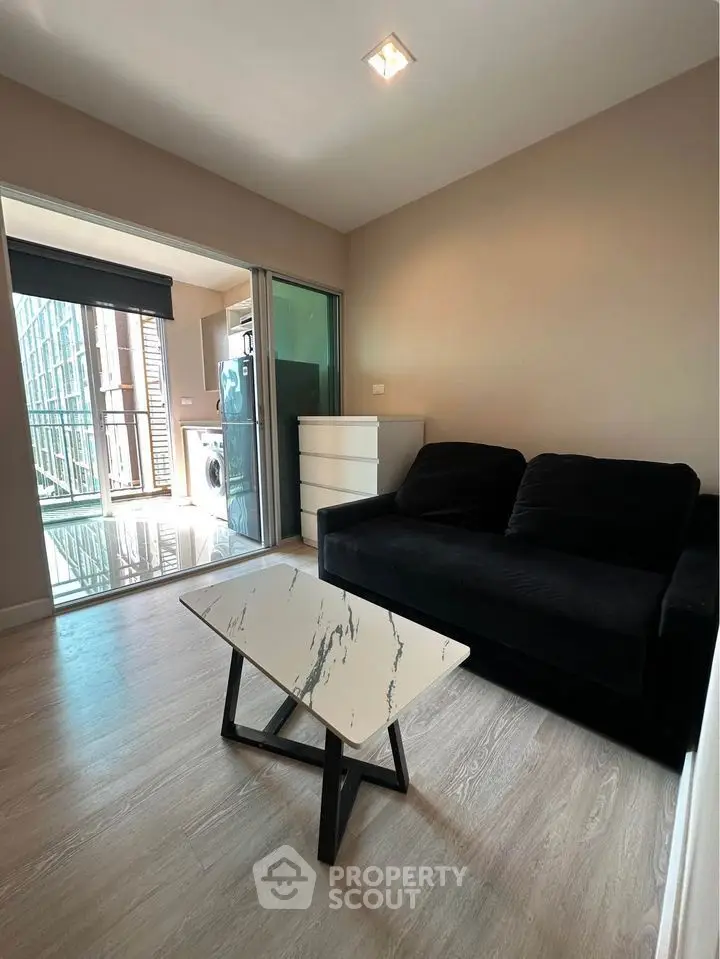 Modern living room with sleek black sofa and marble coffee table, adjacent to a bright balcony area.