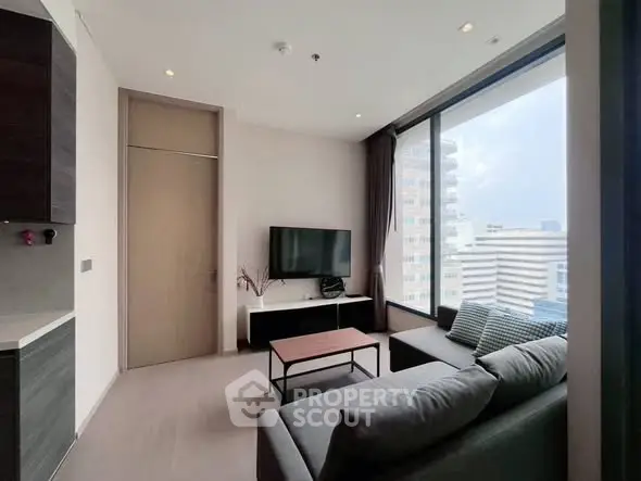 Modern living room with large window and city view, featuring sleek furniture and neutral tones.