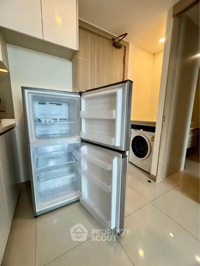 Modern kitchen with open fridge and washing machine, sleek design.
