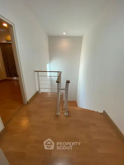 Spacious hallway with wooden flooring and modern railing, leading to a cozy room.