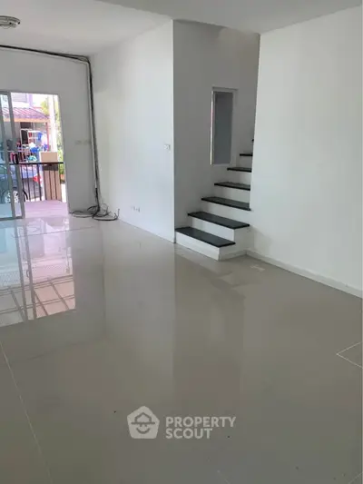 Spacious modern living room with sleek staircase and glossy tiled floors, perfect for contemporary living.