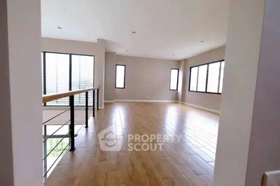 Spacious empty living room with wooden flooring and large windows.