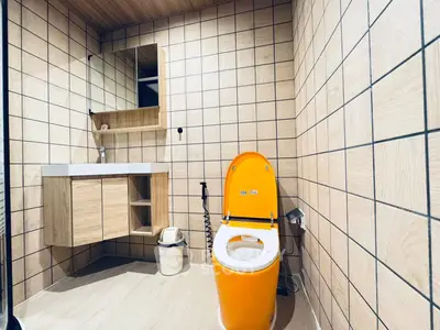 Modern bathroom with unique orange toilet and stylish wooden cabinetry.