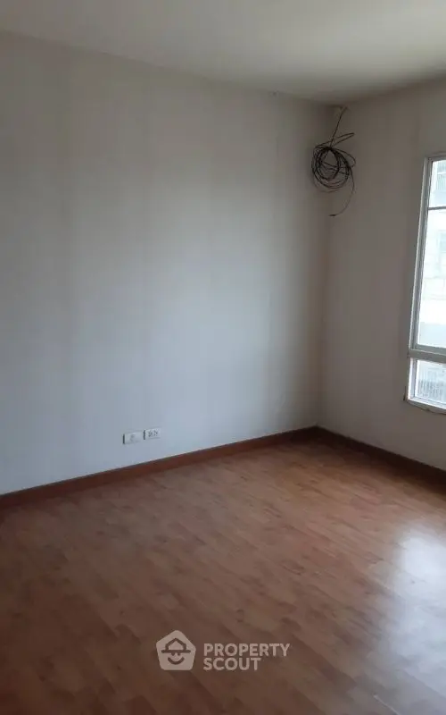 Spacious empty room with wooden flooring and large window, ideal for customization.