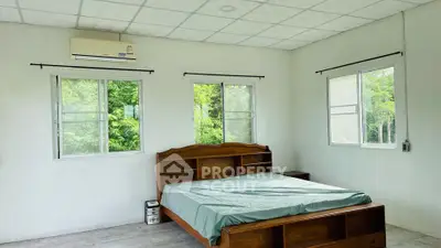 Spacious bedroom with large windows offering ample natural light, complemented by a sturdy wooden bed and a serene green view.