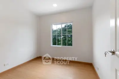 Bright empty room with wooden flooring and large window overlooking greenery.
