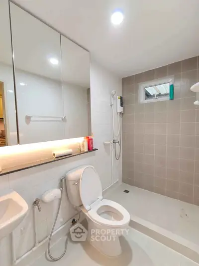 Modern bathroom with sleek fixtures and neutral tiles, featuring a shower and toilet.