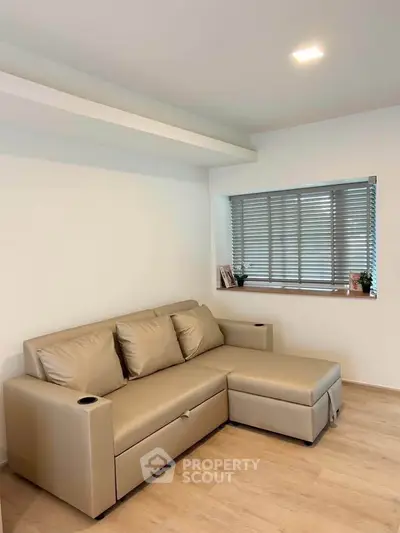 Modern living room with beige sectional sofa and large window with blinds