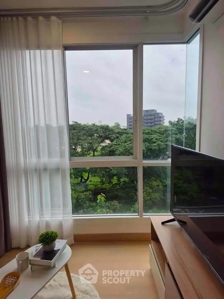 Bright living room with large window offering lush green view, modern decor, and cozy ambiance.
