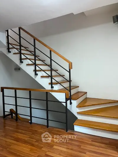 Modern staircase with wooden steps and sleek metal railing in a contemporary home interior.