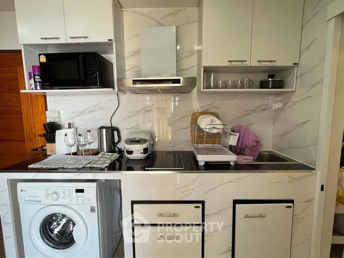 Modern kitchen with washing machine, microwave, and sleek cabinetry in compact layout.