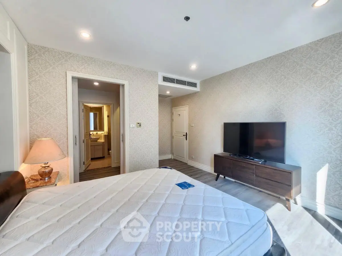 Spacious bedroom with modern decor and ensuite bathroom in luxury apartment.