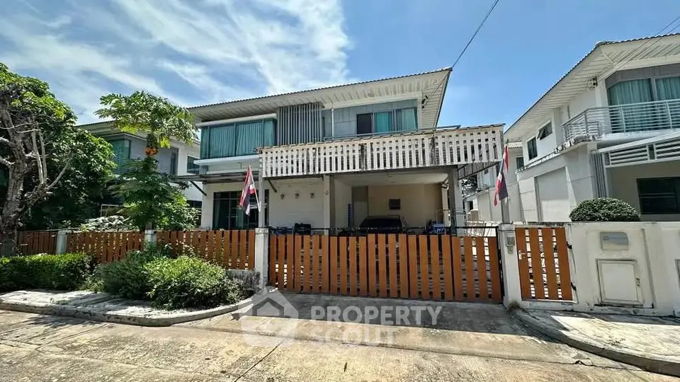 Charming two-story house with wooden fence and lush greenery in a serene neighborhood.