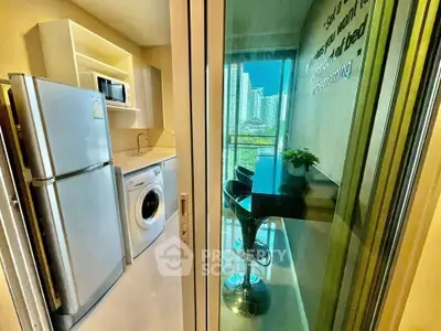 Modern kitchen with balcony view, featuring fridge, washing machine, and breakfast bar.