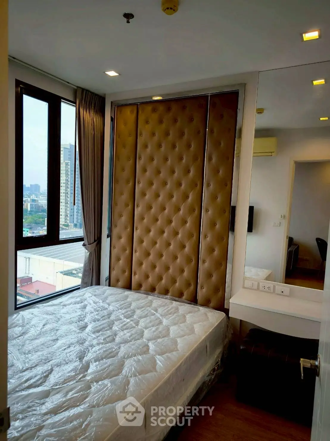 Modern bedroom with large windows and city view, featuring a stylish padded headboard.