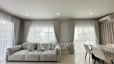 Spacious modern living room with plush sofa and elegant dining area, featuring large windows and natural light.