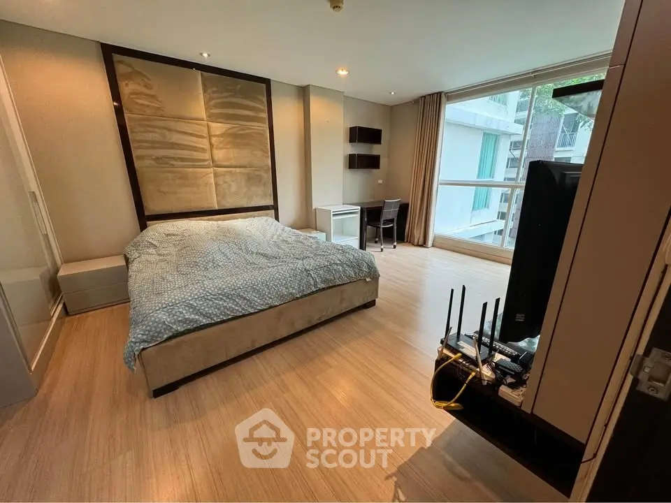 Spacious bedroom with modern decor and large window offering natural light