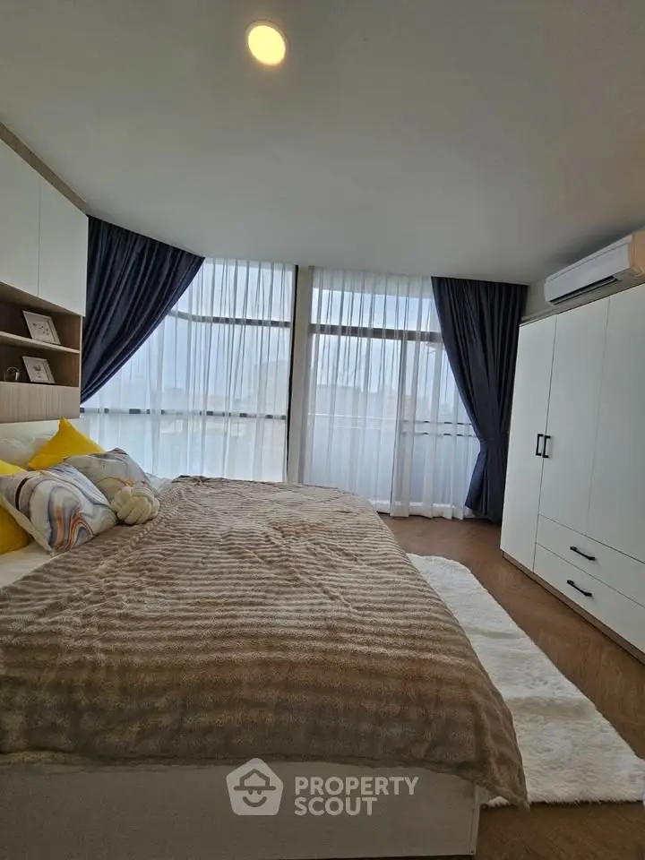 Spacious bedroom with large windows and modern decor, featuring cozy bedding and ample storage.