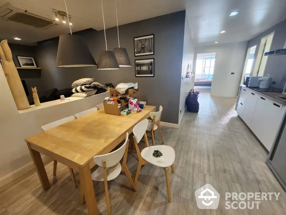 Modern dining area with wooden table, stylish lighting, and open kitchen layout in a cozy apartment.