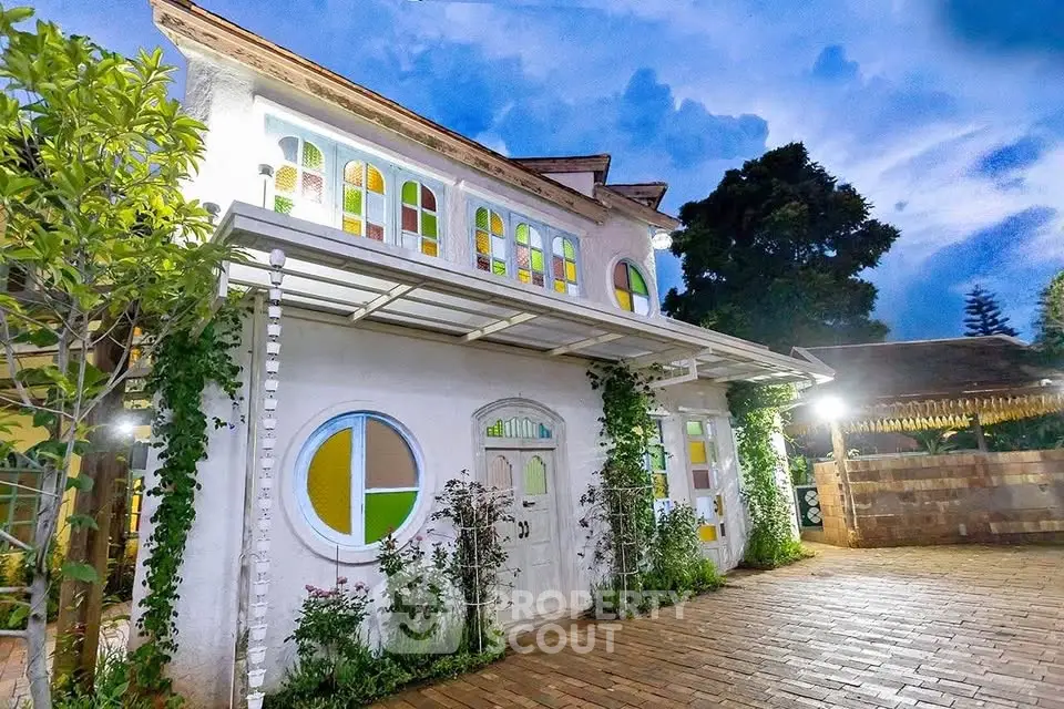 Charming two-story house with colorful stained glass windows and lush greenery, perfect for serene living.