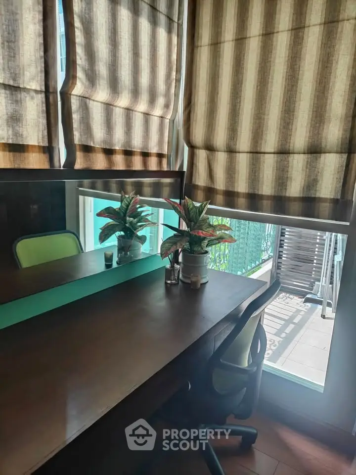 Cozy study room with desk, chair, and potted plants by a window with striped blinds.