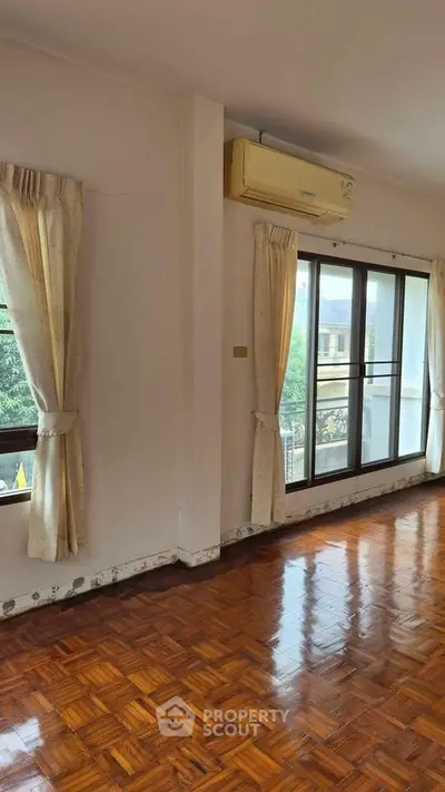Spacious living room with wooden flooring and large windows offering natural light and garden view.
