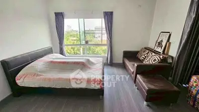Spacious bedroom with large window and cozy seating area in modern apartment.
