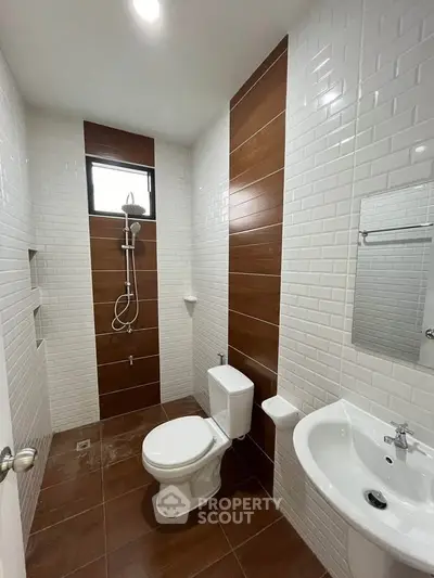 Modern bathroom with sleek white tiles and brown accents, featuring a shower and toilet.