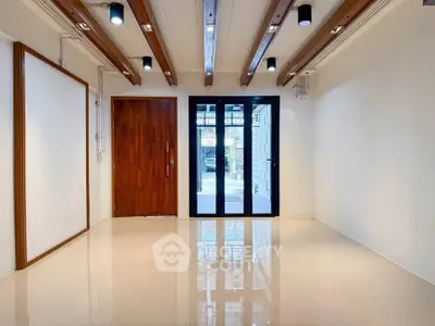 Spacious modern room with wooden beams and glass doors, ideal for versatile living space.