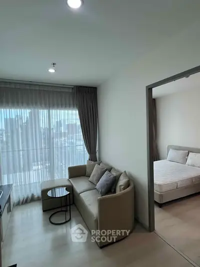 Modern apartment living room with cozy sofa and bedroom view, featuring large windows and natural light.
